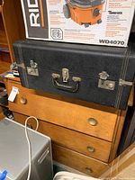 Photo showing the three drawer wooden chest with a black hard case on top, drawers showing signs of damage or misalignment.