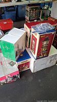 Stacked boxes of Christmas village displays, various sizes and colors showing the packaging and brand labels.