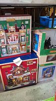 Front view of boxed Lemax Christmas village displays stacked under a table