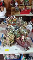Photo showing overall assortment of Christmas village buildings, Santa in car, and bird cage on table.