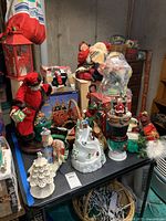Table showing assortment of Christmas figures including Santas, snowman, decorative Christmas trees, and holiday ornaments.