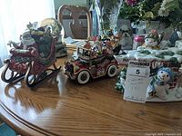 Photo showing three Christmas-themed figurines: a Santa sleigh music box, a vintage car music box with reindeer and Santa, and a snowman teapot with a 'mail' sign handle.