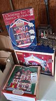 Overall view of boxed Christmas Eve At Santa's Workshop display and other boxed village items with metal train on top.