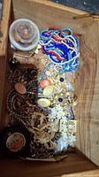 Open wooden box filled with assorted mixed costume jewelry including beaded necklaces, floral brooches, clip-on earrings, and rings, showing the variety and condition of items.
