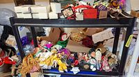 Two shelves filled with assorted dolls and other items including white boxes and packaging materials.