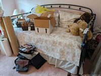 Full view of the daybed showing floral linens, trundle underneath, and assorted boxes and bags on and around the bed.