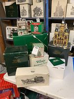 Wide shot of assortment of Dickens Village Series collectible buildings and boxes stacked on table and shelves.