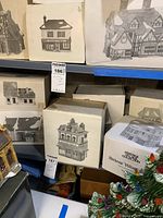 Wide view showing shelf with multiple white boxes containing Dickens Village houses and some partially visible decorations.