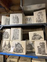 Eleven boxes of Dickens Village Series houses on shelving, some stacked; group overview