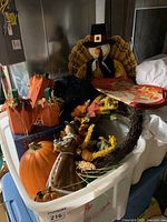 View of assorted fall decorations including pumpkins, scarecrow, turkey figure, and wreath in a bin.