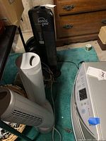 Photo showing three fans and some cords on carpet near furniture, includes black Ionic Pro fan and two other tower fans