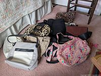 Wide shot of lot showing six handbags of different styles and colors on carpeted floor next to a bed and chair.