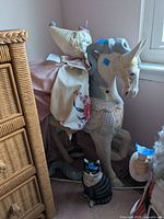 Wooden horse figurine with clown doll behind it on floor near window, with cast iron cat to front right.