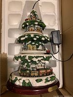 Three-tier Thomas Kinkade electric Christmas tree figurine with village scenes and train, missing top piece, powered by external power adapter.