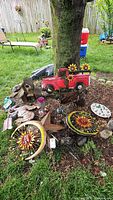 Photo showing multiple metal lawn and garden decor items including sun and moon wall hangings, red pickup truck decoration, multi-tier wooden birdhouse, birds, and rooster weathervane.