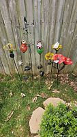 Wide view showing 10 colorful lawn decor pieces including glass flowers, bird figure, gnome, solar light stakes, and metal wind vane