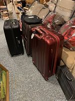 Photo showing multiple luggage pieces in various styles and colors, including red and black hard shell suitcases, and soft backpacks, stacked near furniture and pillows.