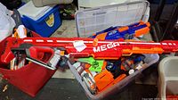 Two containers with assorted Nerf dart blasters including a large red Nerf Mega shooter and multiple orange dart magazines.