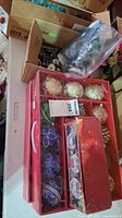 Two boxes with decorative Christmas ball ornaments in gold, blue, red, and purple colors with intricate designs and some glitter detailing.