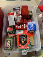 Overhead view of a plastic tub holding multiple Christmas ornaments in original boxes and packaging.