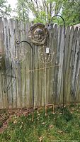 Two decorative scarecrows on shepherd hooks and a ceramic plaque hanging on wooden fence.