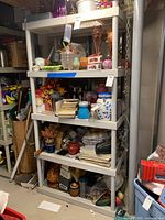 Full view of white plastic shelving unit with various household items on shelves in a basement or storage room setting. Shelving unit has five shelves and stands upright with support braces on the back and sides. Shelves contain mixed items but are not included in the sale.