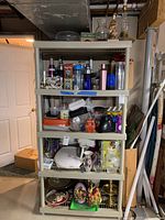 Beige plastic shelving unit with five shelves stocked with assorted household items including bottles, containers, glassware, an appliance, and decorative objects.