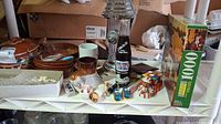 Shelf with various ceramic bowls, mugs, small glass items, a Rubik's Cube style puzzle cube, and a glass Coke bottle decanter with label 'Fire Plug'