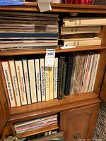 Shelf showing vertical boxed music collections and stacked vinyl records on a wooden shelf unit