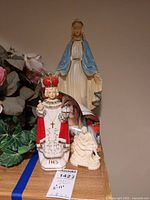 Set showing Infant Jesus of Prague statue, Pieta statue, and Our Lady of Fatima statue with plants in background.