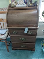 Front view of roll top desk showing its wood finish and the three drawers with decorative metal handles, with some scratches and wear visible.