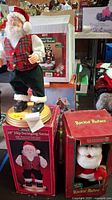 Hip Swinging Santa figurine standing on box along with boxed Rockin' Rollers Santa and a boxed musical holiday house in the background.