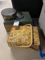 Woven basket-style sewing box with patterned fabric lid alongside vintage green metal sewing box and round decorative metal tin, items grouped closely to show full lot.
