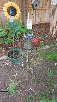 View of two metal shepherd's hooks standing in garden soil with a hanging plastic flower basket on one and a candle holder on the other