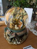 Front view of the nativity snow globe showing Mary, baby Jesus, wise men, and angel inside the glass dome, with detailed base.