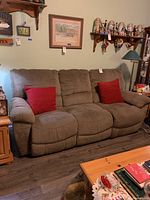 Front view of brown fabric three-seat sofa with two red throw pillows, showing attached cushions and reclining seats on the ends.
