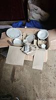 Photo showing box with unfolded cardboard holding multiple stoneware items including plates, some stacked, cups and bowls with floral design.