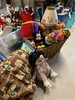 Wicker basket of assorted stuffed animals and baby toys, nearby vintage sleeping bag, and handmade doll