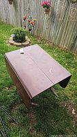 Photo of entire wooden table folded with metal clawed feet on grass, showing overall condition and folds.