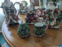 Front view of three Santa Claus themed teapots and Spode Christmas tree cream and sugar on wooden table