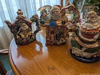 Three Fitz and Floyd Santa Claus themed teapots arranged on a wooden table near window light.