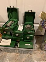 Twelve green boxes containing miniature pewter steins stacked inside a plastic container.