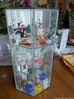 Full view of hexagonal mirrored plexiglass display cabinet showing multiple glass artisan figures and souvenir thimbles inside