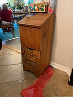 Wooden vegetable bin with three compartments labeled for storing potatoes, apples, and onions placed on floor in corner of room.