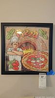 Front view showing framed pizza box top art with the chef, pizza oven, pizza, tomatoes and basil leaves.