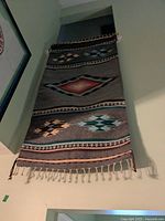 Wool tapestry wall hanging displayed vertically on wall showing geometric patterns and fringed edge.
