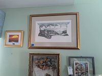 Three framed artworks on wall: large landscape print, smaller sunset print, and dried flower canvas