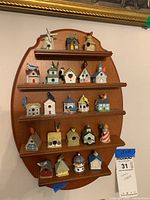 Full view of the oval wooden shelf mounted on wall, displaying 22 miniature birdhouse thimbles arranged on five narrow shelves.