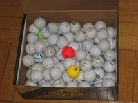 Box containing large quantity of used golf balls, mostly white with few colored