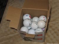 Open box filled with mixed white golf balls showing Titleist, Callaway logos